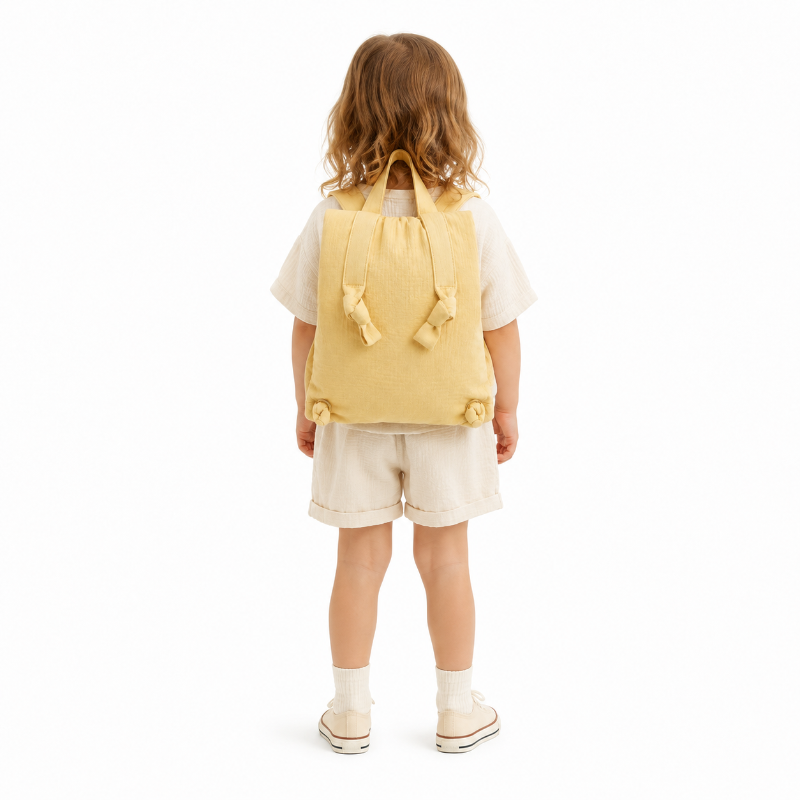 Enfant de maternelle portant un sac à dos jaune en mousseline gaufrée avec bretelles nouées, vue de dos.