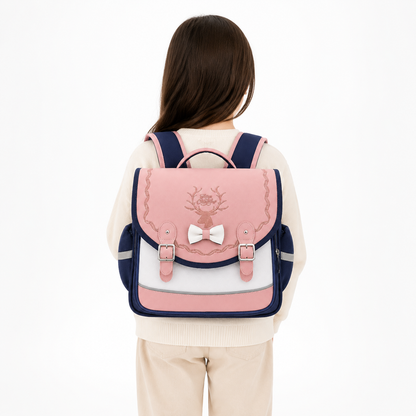Enfant de CP portant un cartable rose et bleu marine avec cerf brodé, nœud blanc et boucles argentées, vue de dos