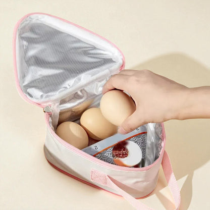 Main d’un enfant rangeant un œuf dans un sac gouter isotherme rose avec aliments à l’intérieur.