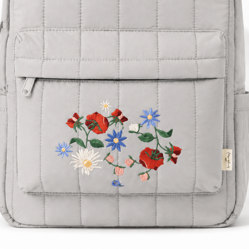 Détail du bouquet floral brodé, du matelassage et des coutures du sac à dos enfant gris perle