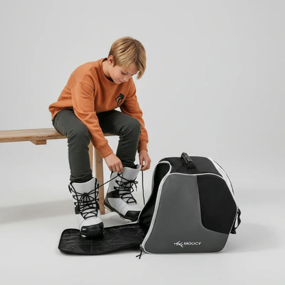 Enfant mettant ses chaussures de ski à côté d’un sac de ski enfant avec compartiment dédié
