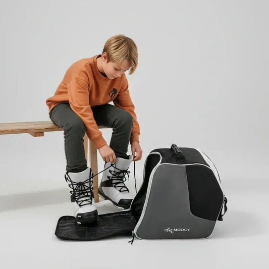 Enfant mettant ses chaussures de ski à côté d’un sac de ski enfant avec compartiment dédié
